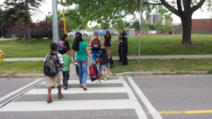 A picture of children using a crosswalk on the way to school with the help of adults.