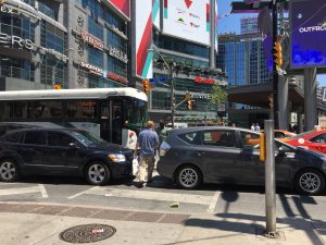 A picture of a man trying to cross a street using a crosswalk blocked by cars at Yonge and Dundas