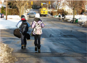 A picture of two children walking on a street without sidewalks on a snowy day.