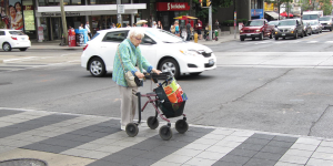 A picture of an old woman using a crosswalk with a mobility device